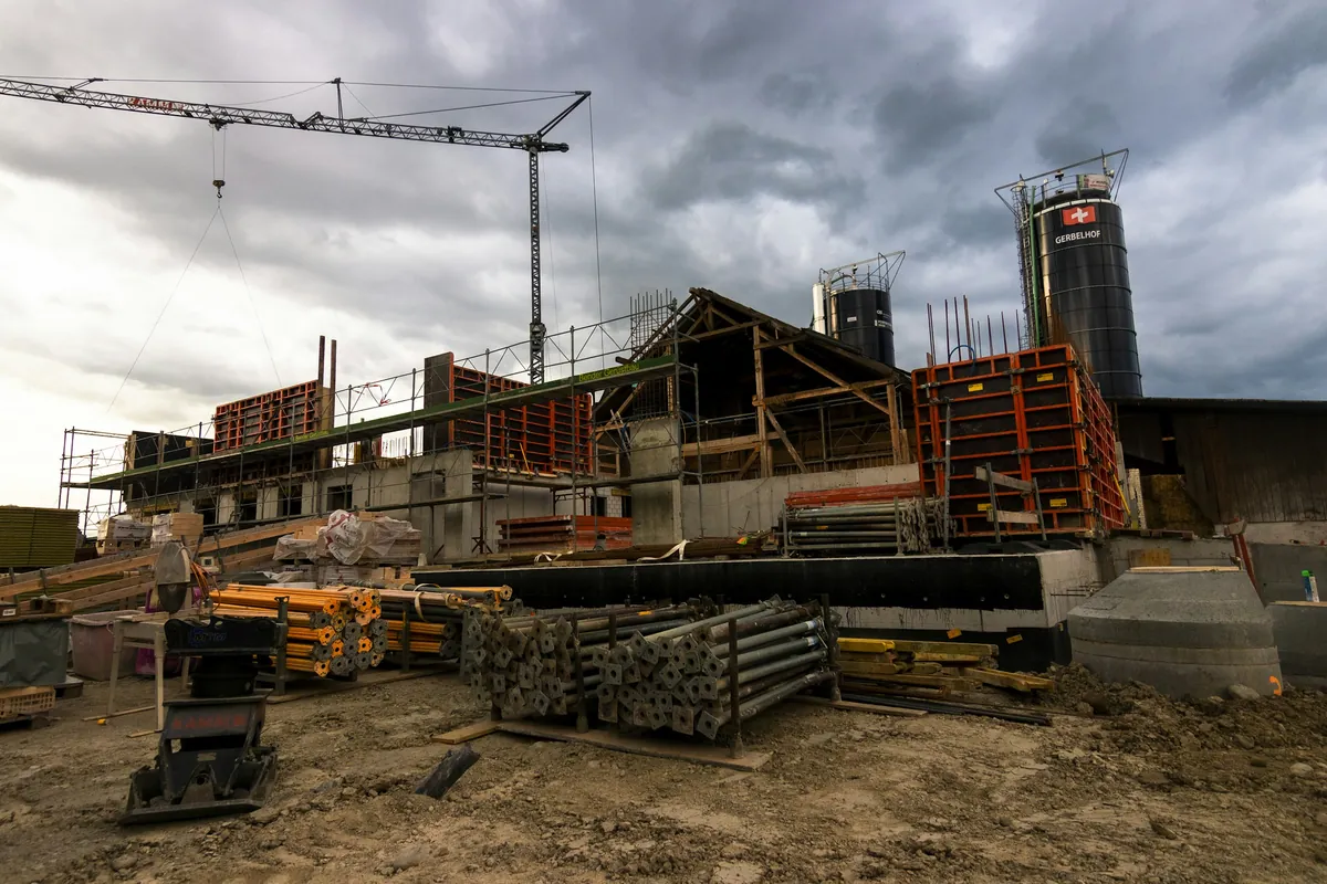 Active construction job site with materials staging and a tower crane under a cloudy sky