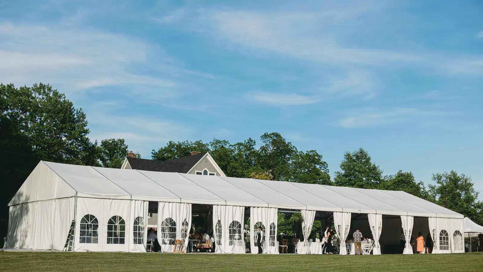 White frame tent with window sidewalls set up on a lawn for a corporate event