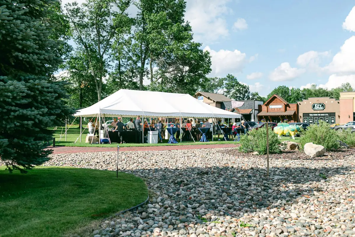 Guests gathered under a white frame tent on a lawn beside local shops