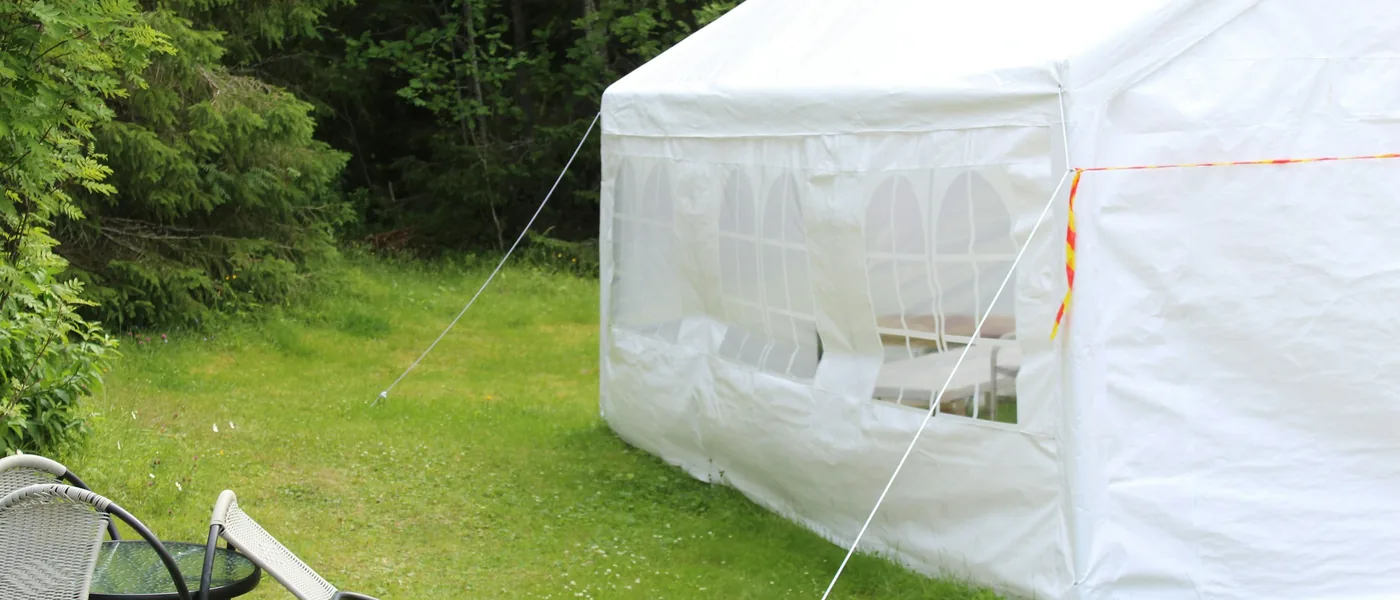 White frame tent with window sidewalls set up on a backyard lawn