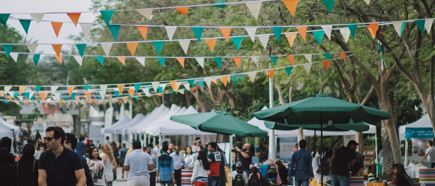 Multi-tent vendor event with tents and umbrellas laid out along a tree-lined walkway