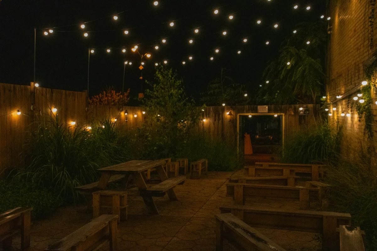 Courtyard patio with wooden picnic tables under string lights at night