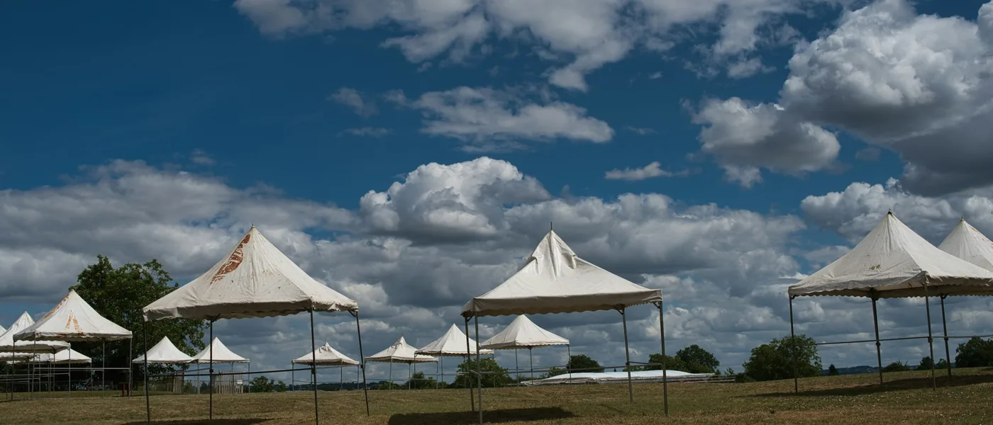 Peaked white tents standing in an open field under a windy cloud-filled sky