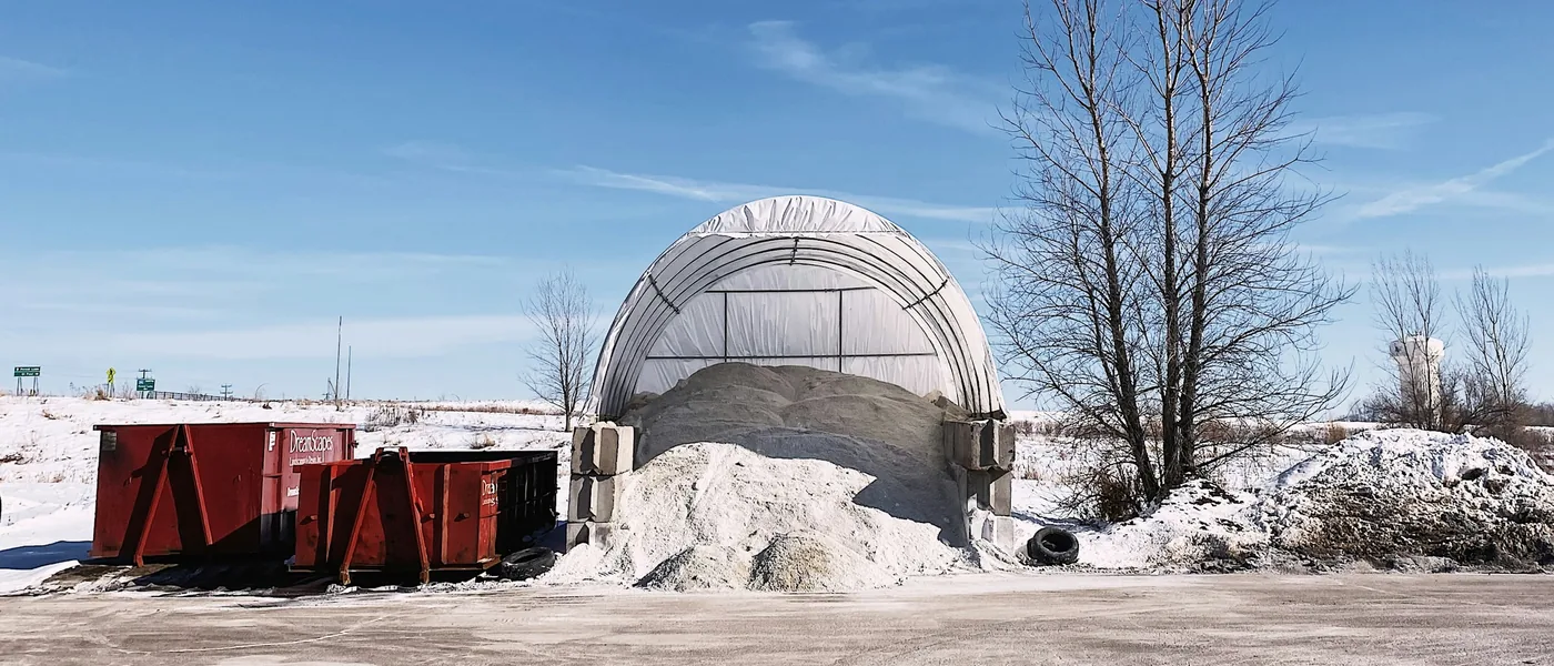 White fabric storage structure anchored with concrete block weights in a snowy commercial yard