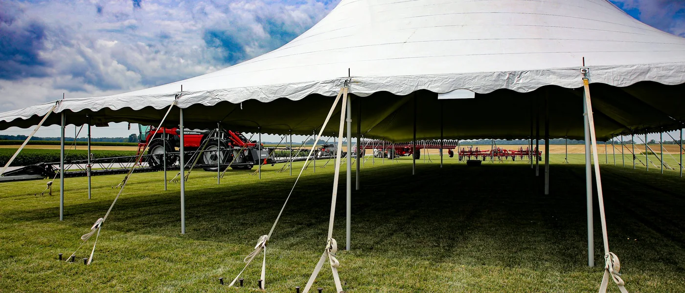Large white pole tent anchored with tension straps and stakes on an open grass field