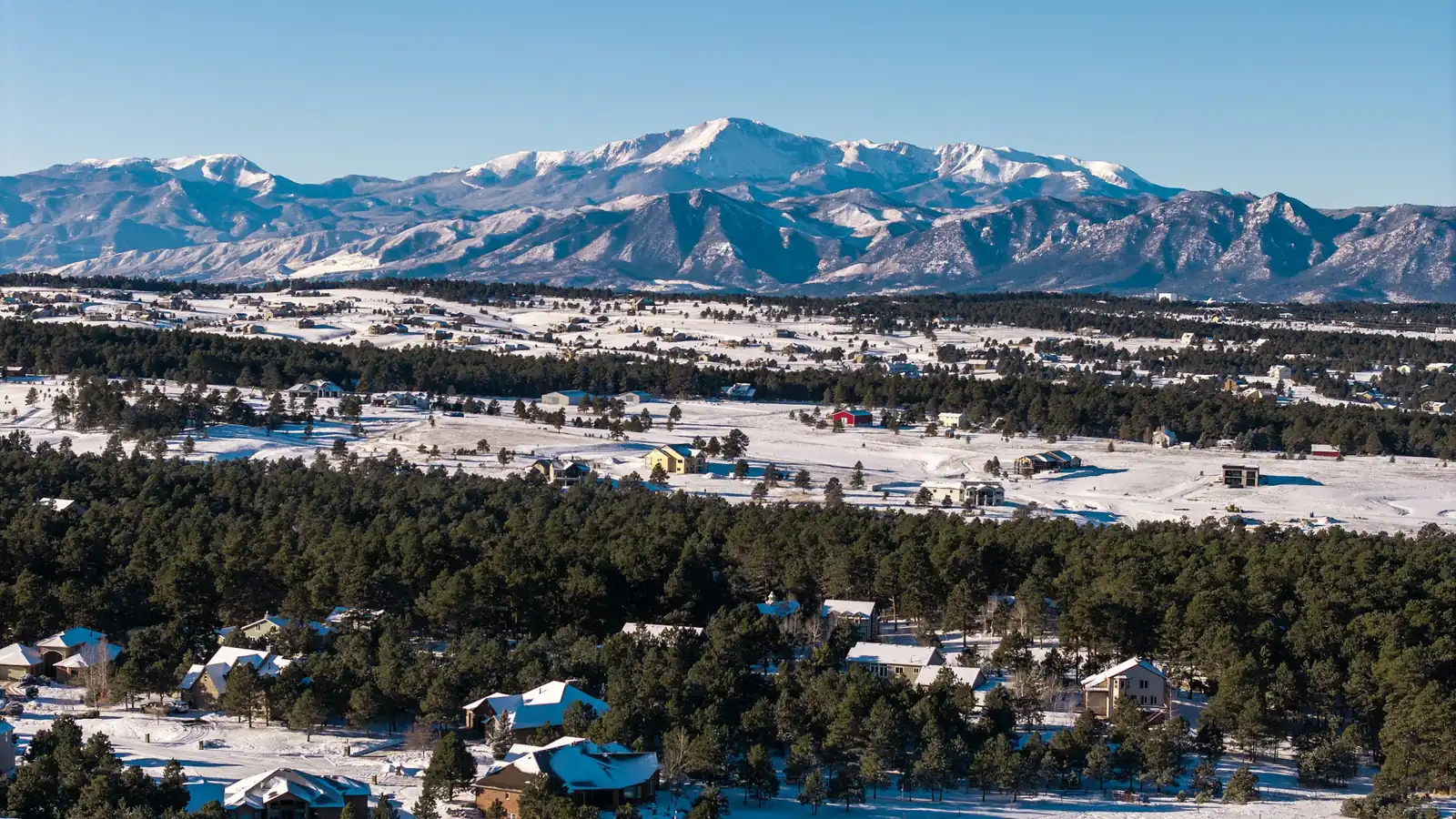 Pikes Peak rising above snow-dusted neighborhoods and pine forest in the Colorado Springs area
