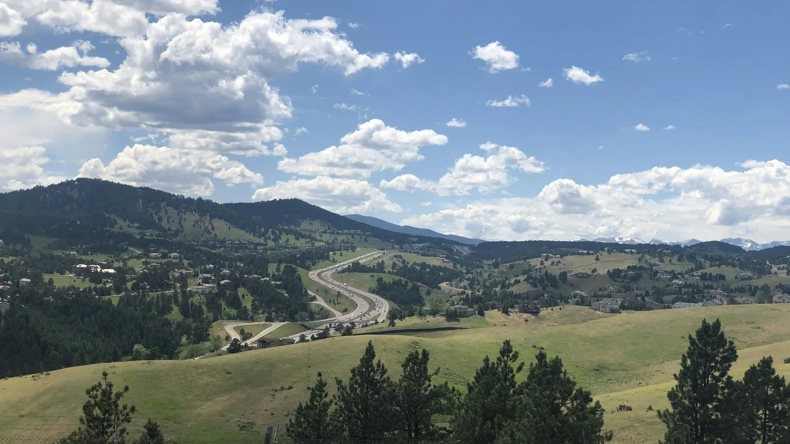 Green foothills and mountain neighborhoods outside Golden, Colorado under a partly cloudy sky