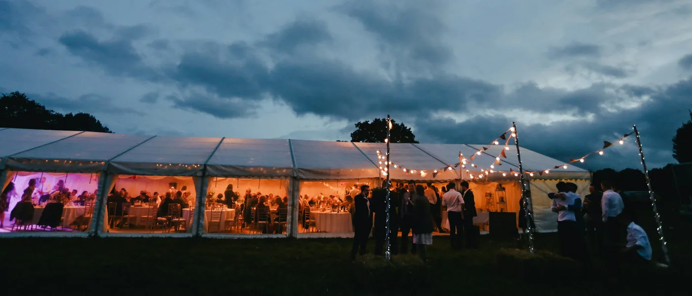 Frame tent wedding reception glowing with string lights at dusk